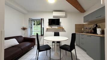 A compact living space with a kitchenette, a dining area with a round table and chairs, a brown sofa, and a television mounted on the wall.