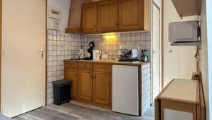 A compact kitchen with wooden cabinets, a small refrigerator, a microwave, and a tiled backsplash. - Alhambra - Studio Cosy (Saint-Martin-d'Uriage)