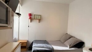 A small, compact room with a bed, a small table, and a shelf with a lamp and picture frame. - Alhambra - Studio Cosy (Saint-Martin-d'Uriage)