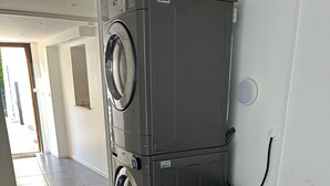 A compact laundry room with a stacked washer and dryer, a dark-colored sofa, and a tiled floor. - Firmament - Studio (Saint-Martin-d'Uriage)