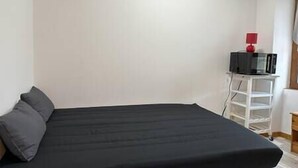 A room with a bed, a small white table with a red lamp, and a white air conditioning unit on the wall. - Firmament - Studio (Saint-Martin-d'Uriage)