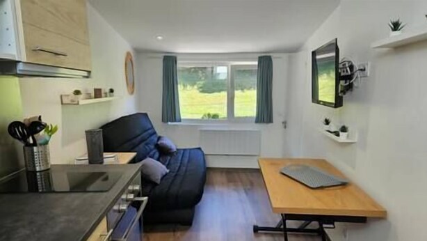 Une pièce compacte comprenant un coin cuisine, un lit, une petite table et une fenêtre avec des rideaux.