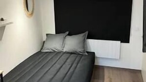 Une chambre à coucher avec un lit, une tête de lit noire, un mur blanc et un plancher en bois.