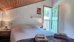 A bedroom with a large bed, a nightstand, a lamp, and a window with a view of greenery. - Ispahan - Grand Duplex Avec 2 Chambres Indépendantes (Saint-Martin-d'Uriage)