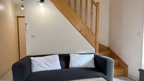 Une pièce avec un canapé noir, un escalier en bois et un mur blanc.