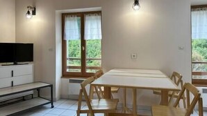 Une pièce comprenant une table et des chaises en bois, un téléviseur et des fenêtres avec des rideaux.