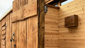A wooden cabin with a rustic design, featuring a wooden door with metal handles and a white toilet. - Walltree House Glamping - Bell Tent (Brackley)