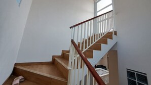 Un escalier avec des marches en bois et des rampes blanches, menant à un palier doté d’une fenêtre et d’un panier blanc.
