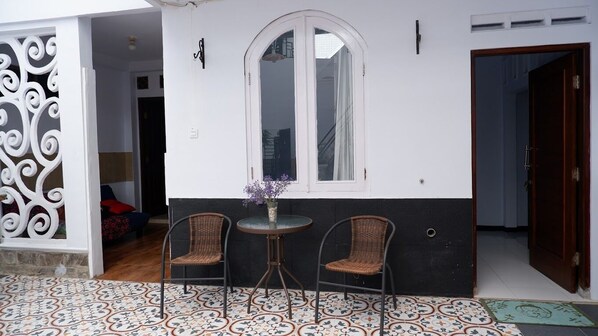 Una habitación con exterior blanco y negro, un ventanal arqueado grande, dos sillas de mimbre, una mesa redonda pequeña con un florero y un suelo estampado.