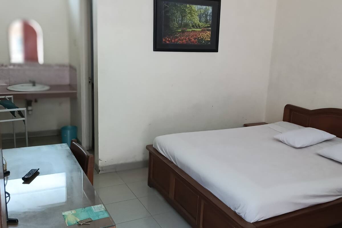 A bedroom with a wooden bed, a bedside table, a mirror, and a sink in the adjacent bathroom.