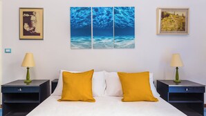 Habitación de hotel con una cama, dos mesitas de noche, dos lámparas y tres cuadros en la pared.
