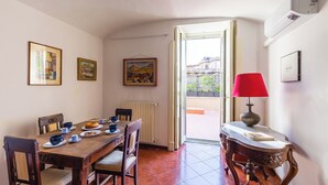 Un comedor con una mesa de madera preparada para cuatro, sillas y una lámpara roja sobre una mesita auxiliar.