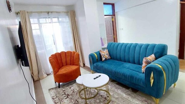 Ein Wohnzimmer mit einem blauen Sofa, einem orangefarbenen Sessel, einem weißen Couchtisch und einem gemusterten Teppich.