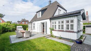 A two-story house with a patio area, a dining set, and a garden.