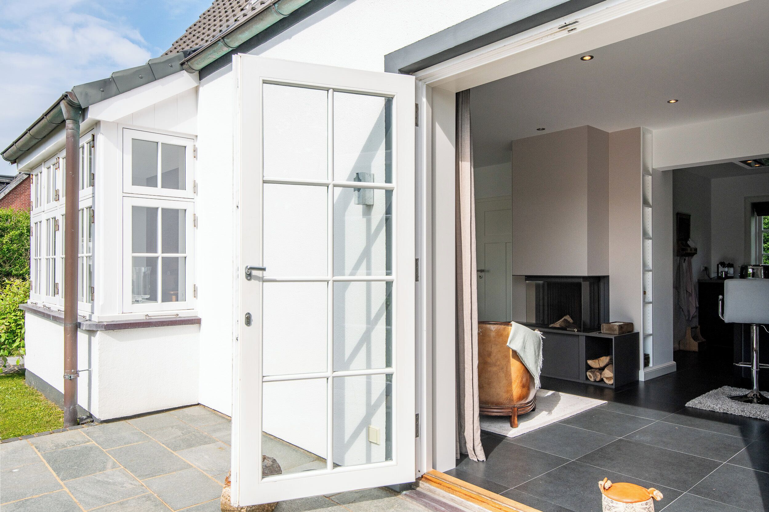 A modern house with a large open door leading to a living area with a fireplace, a sofa, and a dining table.
