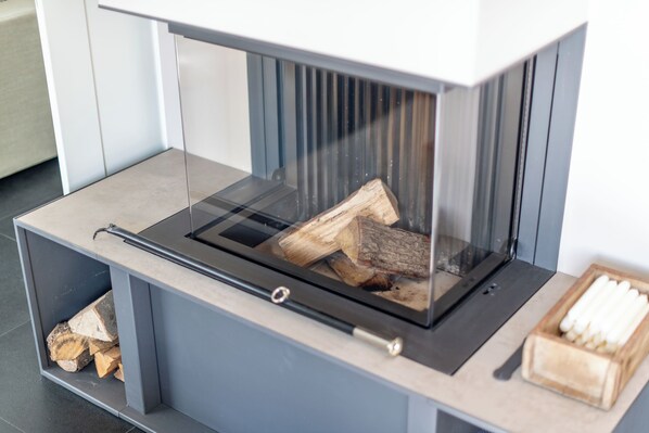 A modern fireplace with a glass enclosure, a built-in shelf for logs, and a wooden box with items on the right side.