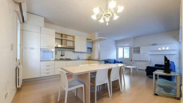 Una cucina moderna con mobili bianchi, un'isola centrale e un lampadario.