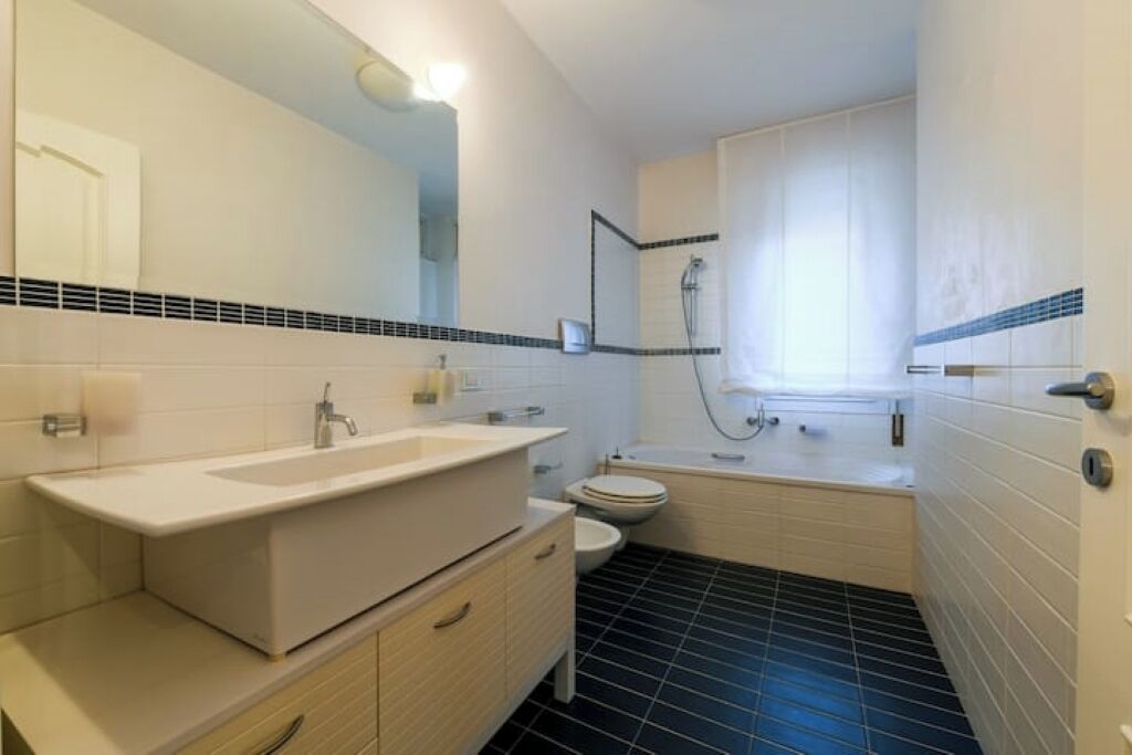 Une salle de bain moderne avec un grand miroir, deux lavabos, des toilettes et une baignoire.