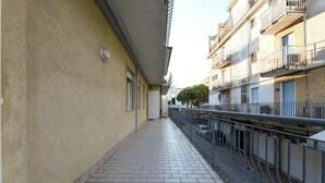Un corridoio stretto con pavimento piastrellato, ringhiere in metallo e una fila di finestre su un lato.