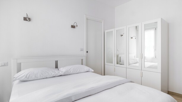 A minimalist bedroom with a large bed, white walls, and a wardrobe with mirrored doors. - A pochi passi dal Mercato delle Erbe by Wonderful Italy (Bologna)
