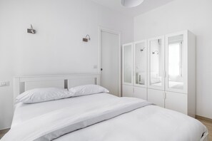 A minimalist bedroom with a large bed, white walls, and a wardrobe with mirrored doors.