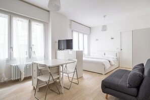 A modern, well-lit room with a white desk, a grey sofa, and a bed. - A pochi passi dal Mercato delle Erbe by Wonderful Italy (Bologna)