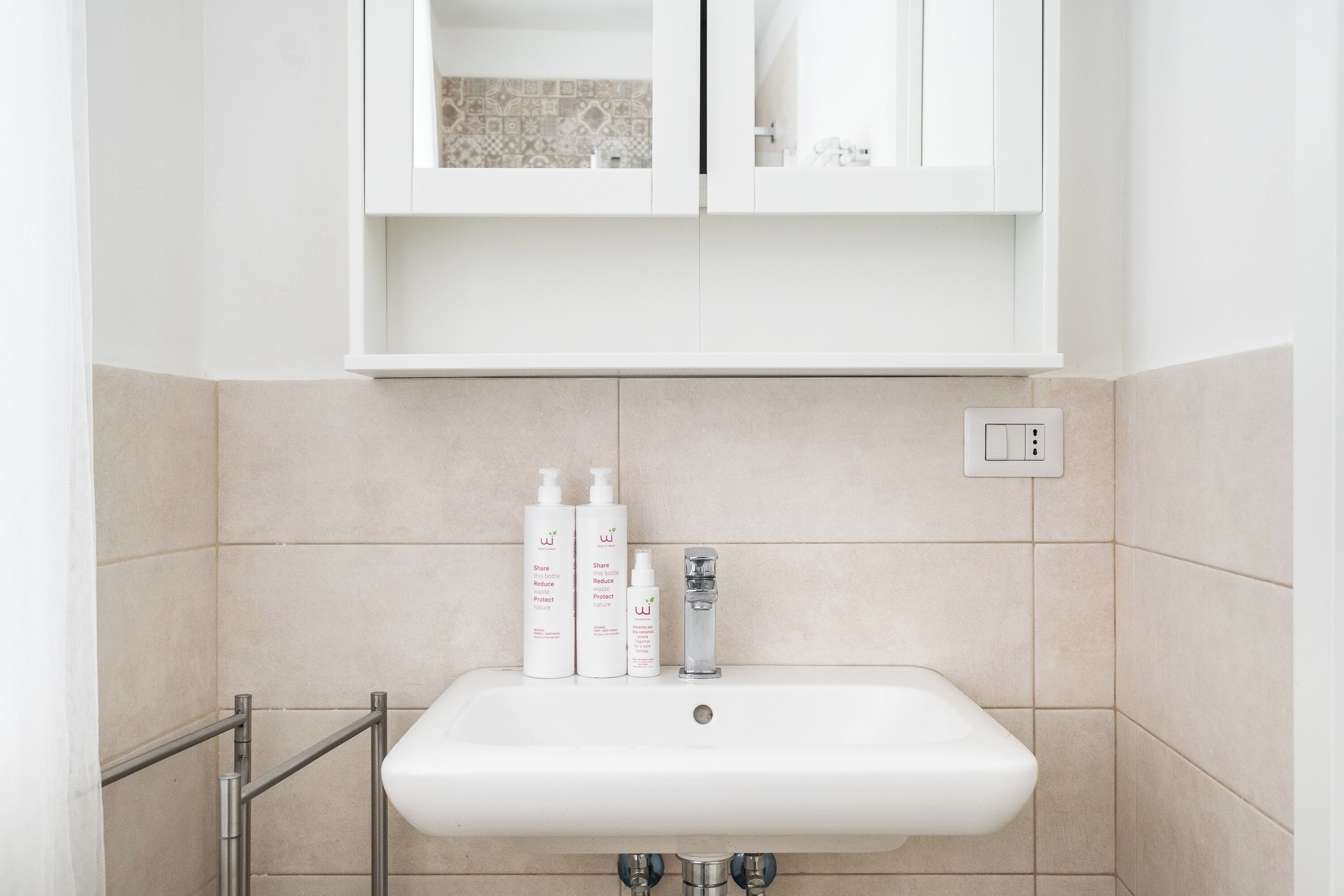 Een badkamer met een witte wastafel, twee shampoos en een spiegelkast erboven.
