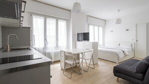 A modern, minimalist room with a kitchen area, a dining table with chairs, a bed, and a sofa. - A pochi passi dal Mercato delle Erbe by Wonderful Italy (Bologna)