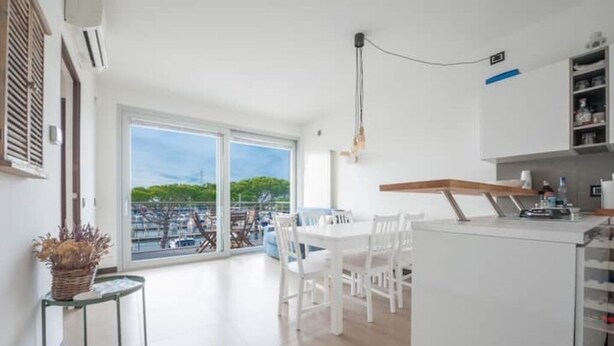 A modern kitchen with a dining area, large windows, and a view of greenery.