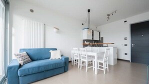 A modern living room with a blue sofa, white dining table, and chairs.