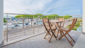 A balcony with a view of a marina, a table, and two wooden chairs.