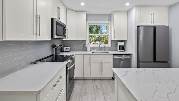 Una cocina moderna con armarios blancos, electrodomésticos de acero inoxidable y un ventanal con vistas a palmeras.
