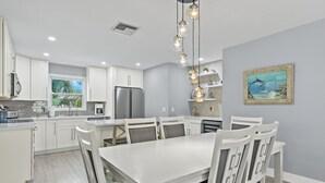 Una cocina moderna con armarios blancos, un refrigerador de acero inoxidable y un comedor con mesa y sillas blancas.