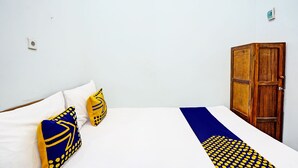 Een slaapkamer met een bed, twee kussens, een houten garderobe en een witte wand.