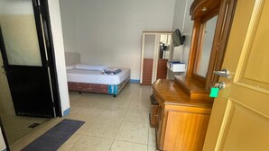 Una camera d'albergo con un letto, una cassettiera in legno, uno specchio e una porta.