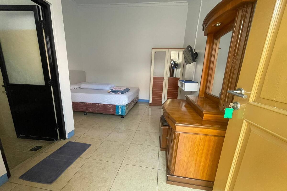 Une chambre d’hôtel avec un lit, une commode en bois, un miroir et une porte.