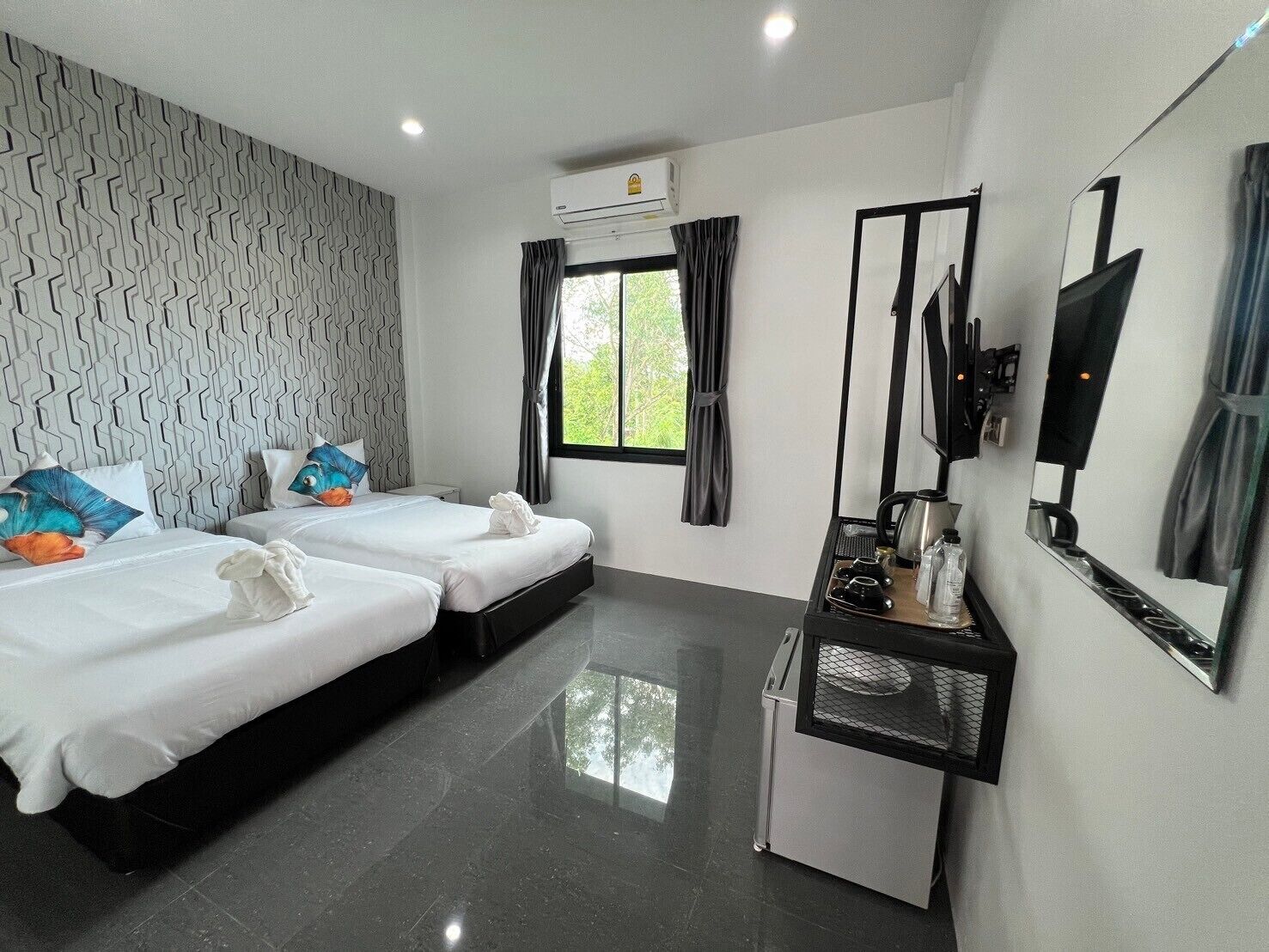 A hotel room with two beds, a small kitchenette, a TV, and a window with curtains.