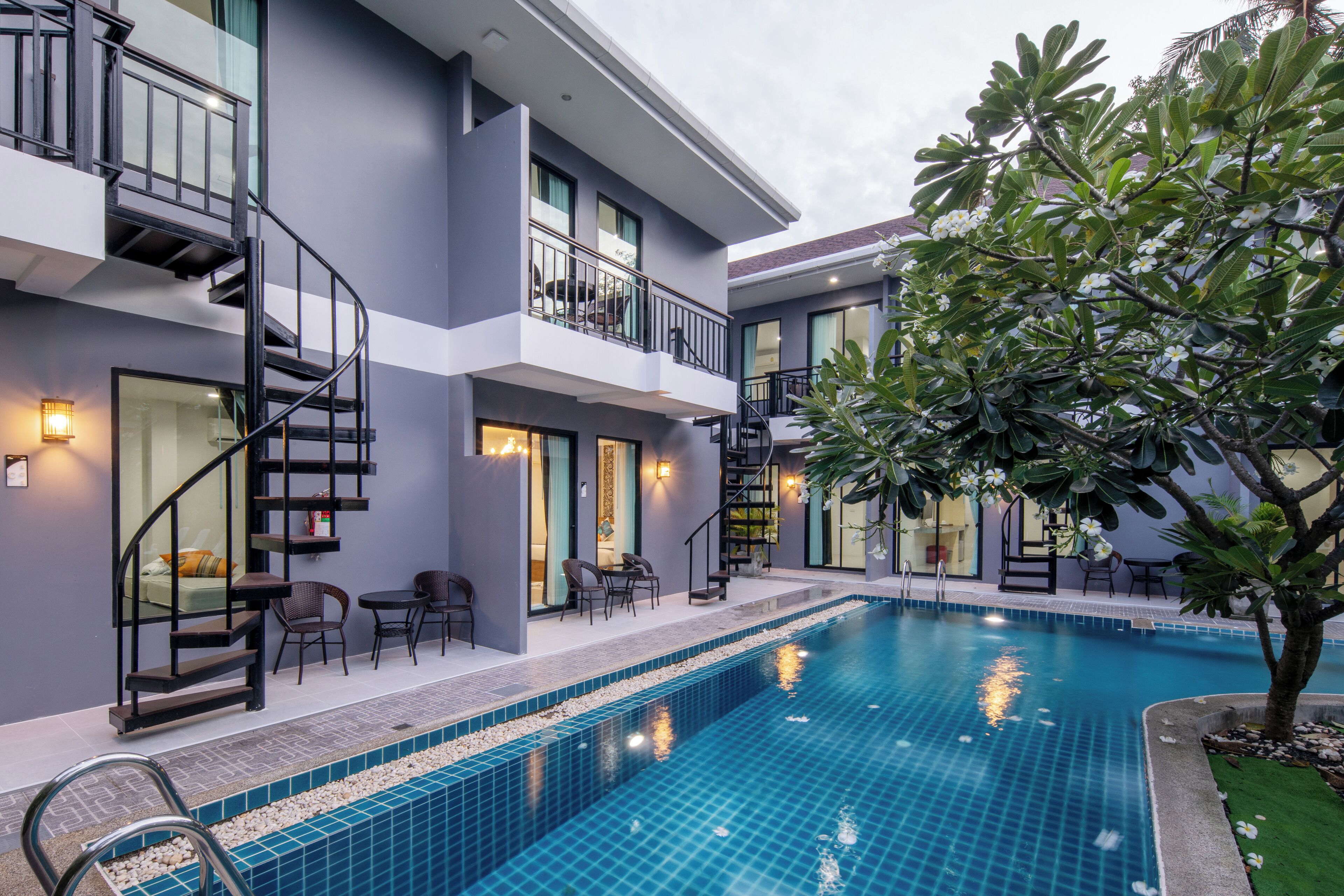 A modern hotel with a swimming pool, outdoor seating, and a staircase leading to the upper floors.