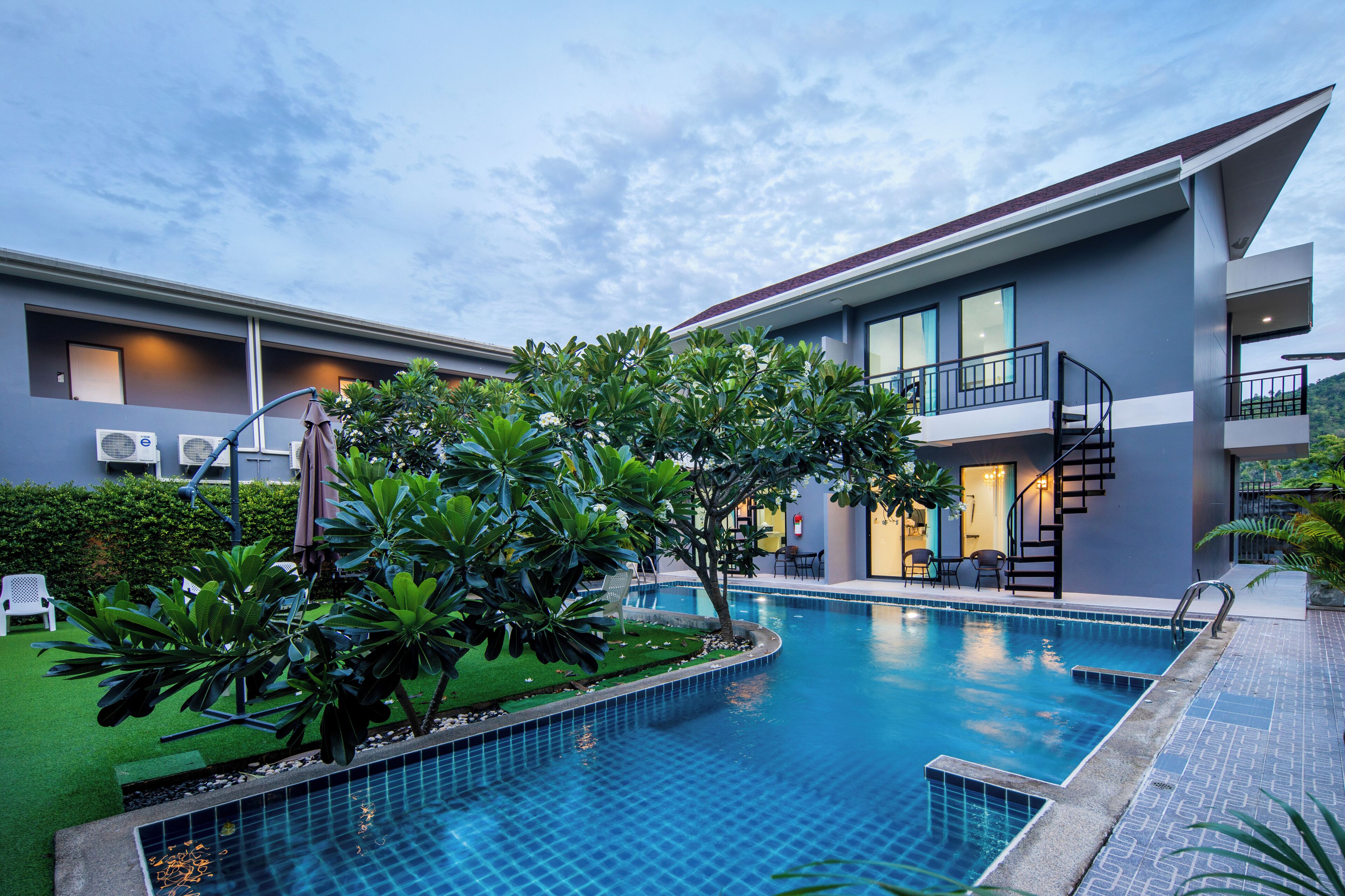 A modern hotel with a swimming pool, outdoor seating, and a staircase leading to the upper floor.