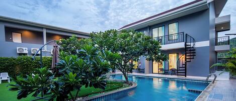 A modern hotel with a swimming pool, outdoor seating, and a staircase leading to the upper floor.