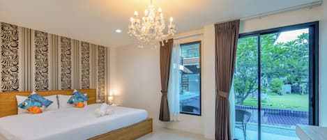 Habitación de hotel con una cama grande, un candelabro, papel tapiz estampado y vistas a un jardín a través de una puerta corrediza de vidrio.