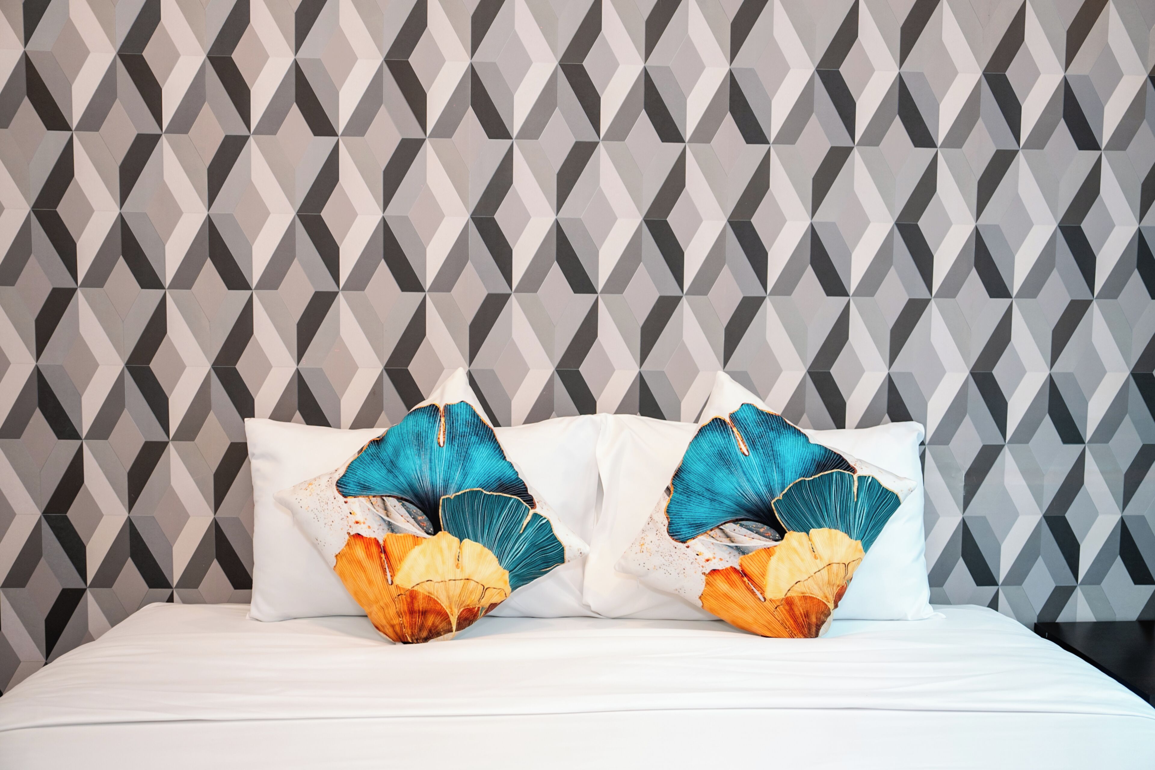 A bed with white sheets and two pillows with tropical leaf designs.