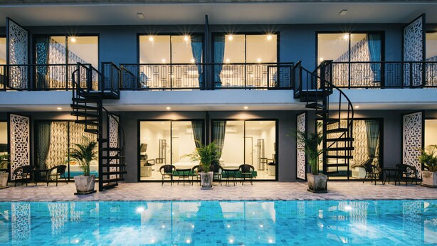 Un hotel moderno con piscina, mobiliario exterior y balcones.