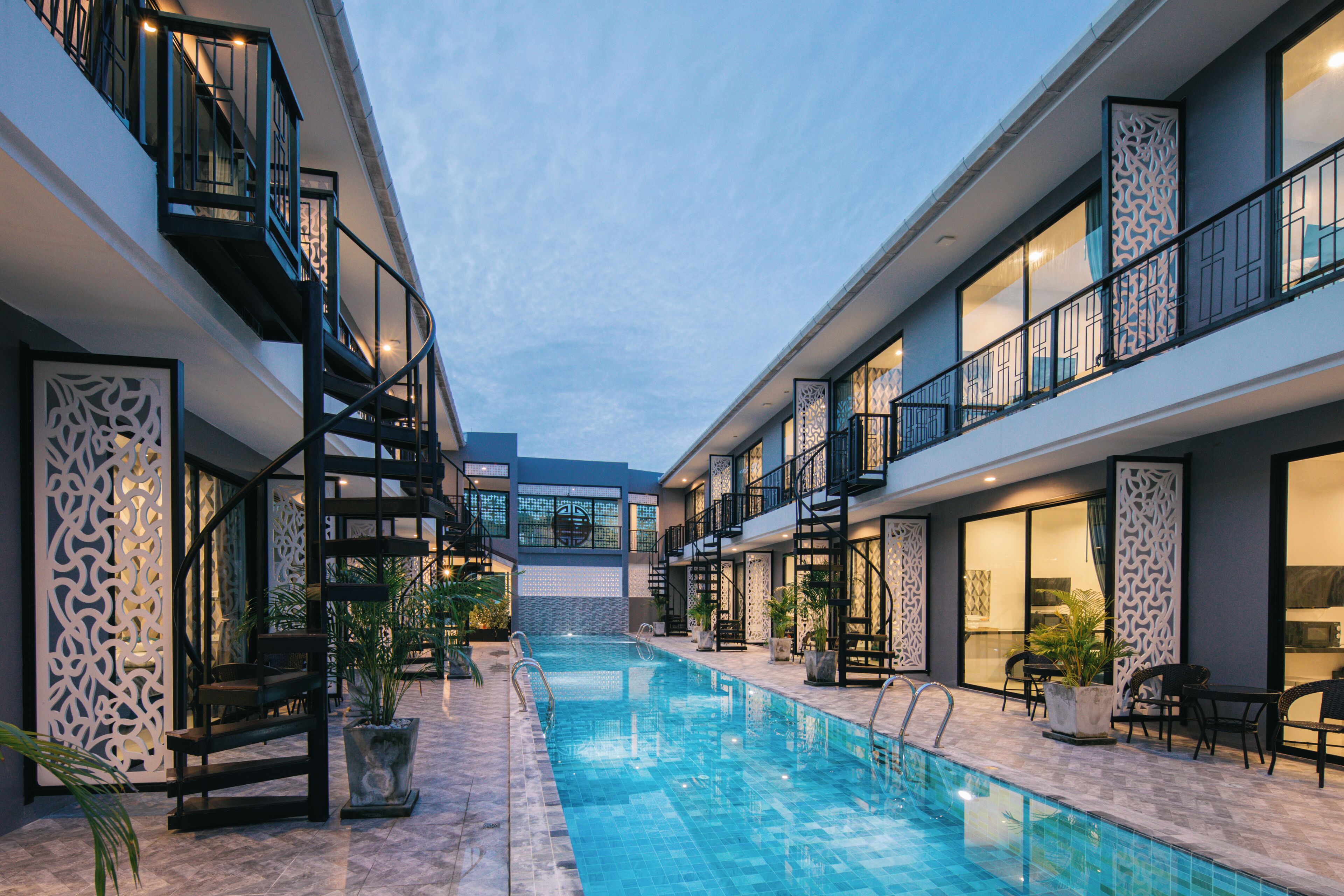 A modern indoor pool area with a clear view of the pool, surrounding lounge chairs, and a staircase leading to the upper floors.