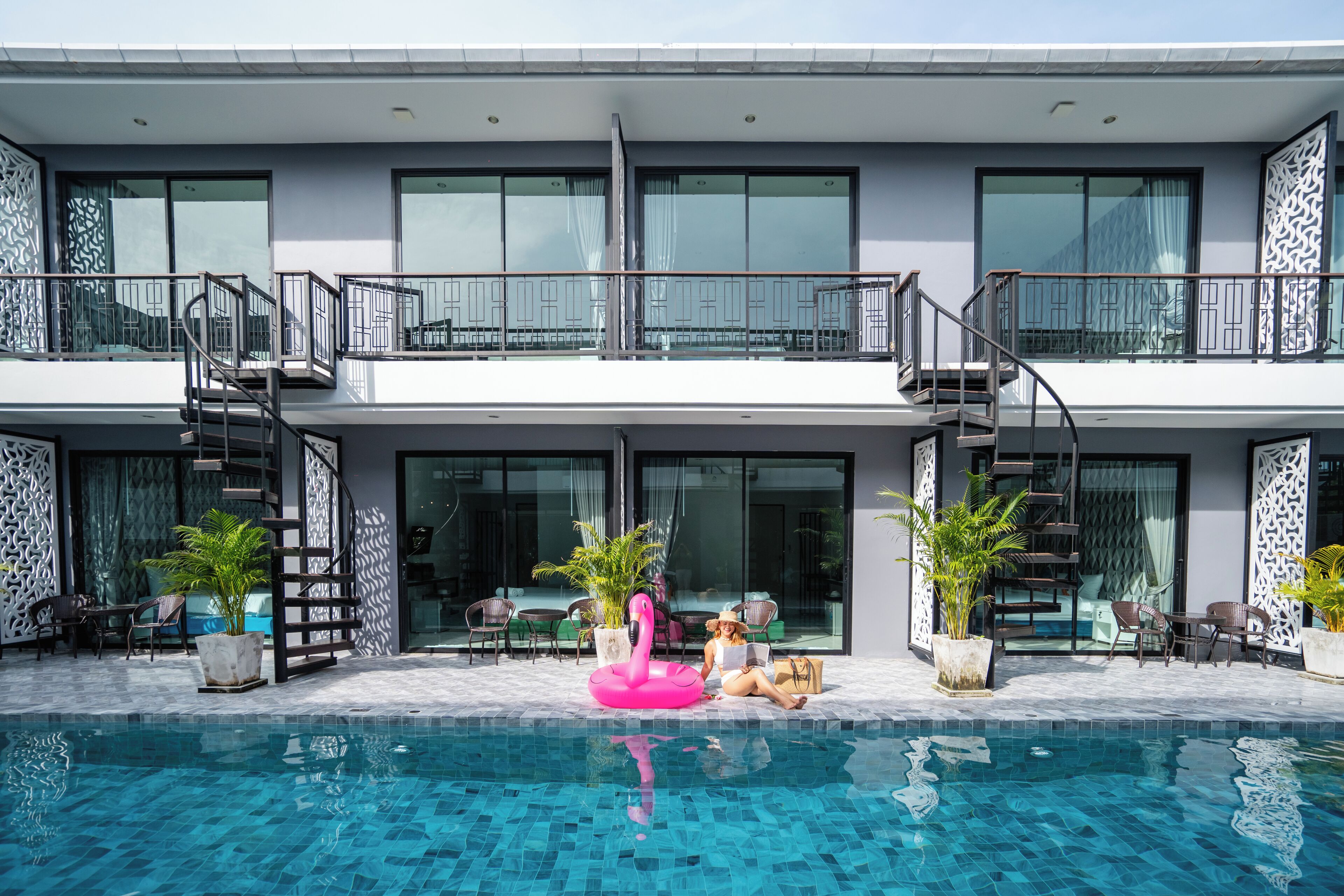 Um edifício moderno de dois andares com piscina, área de estar externa e um boia em formato de flamingos.