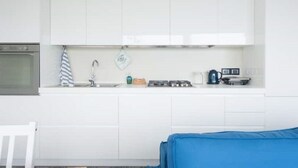 Pieni, käytännöllinen keittiö, jossa on valkoiset kaapit, liesi, pesuallas ja vedenkeitin.