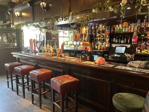 A bar area with stools, a counter with taps, and shelves with bottles. - The Shepherds Rest (Sowerby Bridge)