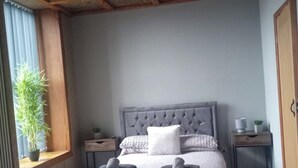A bedroom with a tufted headboard, a bed with rolled towels, a potted plant, and a wooden ceiling. - The Shepherds Rest (Sowerby Bridge)