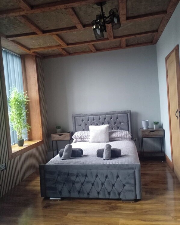 A bedroom with a tufted headboard, a bed with rolled towels, a potted plant, and a wooden ceiling. - The Shepherds Rest (Sowerby Bridge)