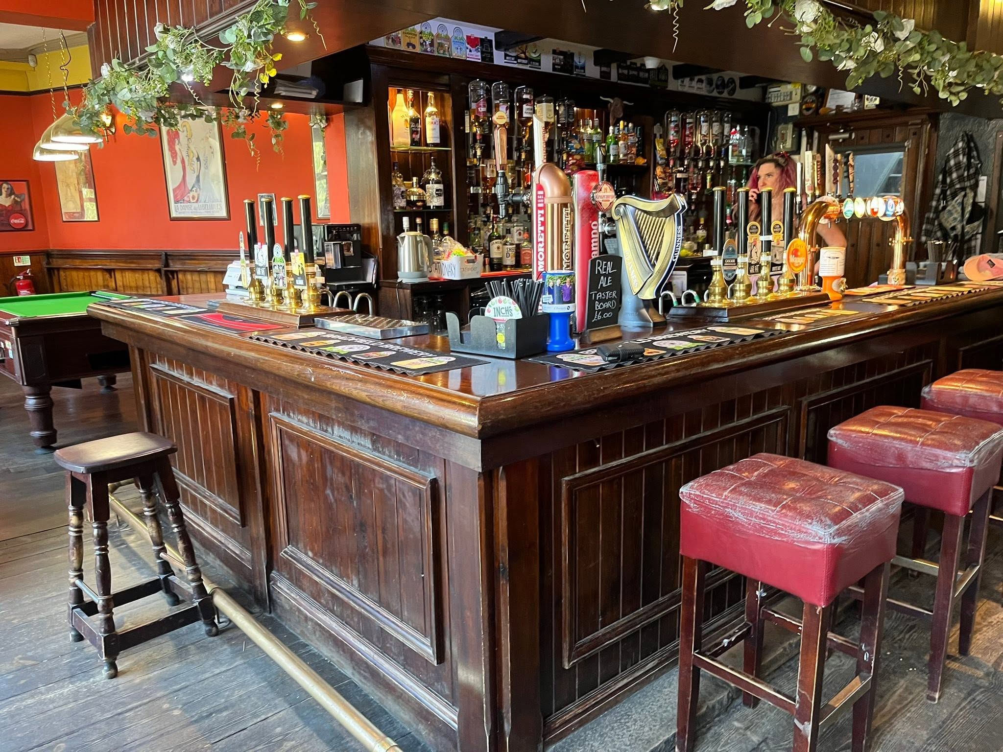 A bar area with a pool table, stools, and a variety of liquor bottles.
